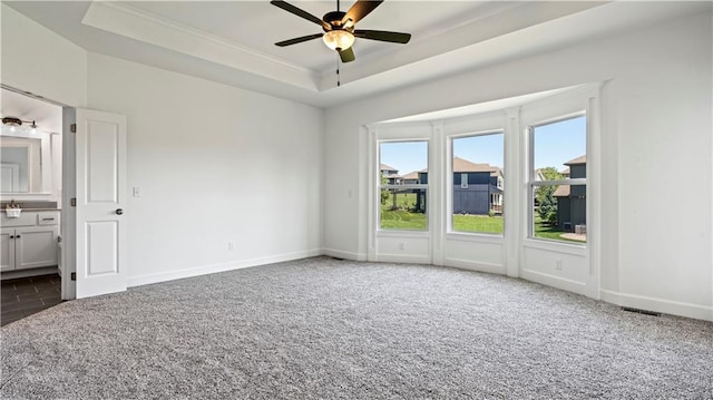 unfurnished bedroom with baseboards, a raised ceiling, connected bathroom, ornamental molding, and dark carpet