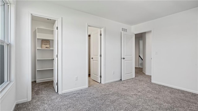 unfurnished bedroom featuring a walk in closet, carpet, a closet, visible vents, and baseboards