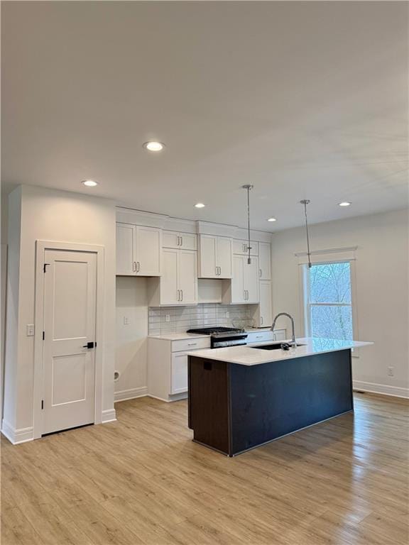 kitchen with pendant lighting, white cabinetry, sink, gas stove, and a center island with sink