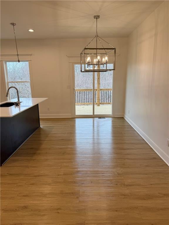 unfurnished dining area featuring wood-type flooring, sink, and a notable chandelier