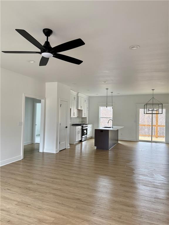 unfurnished living room with ceiling fan with notable chandelier, light hardwood / wood-style floors, and sink