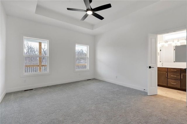 unfurnished bedroom with a tray ceiling, visible vents, light carpet, connected bathroom, and baseboards