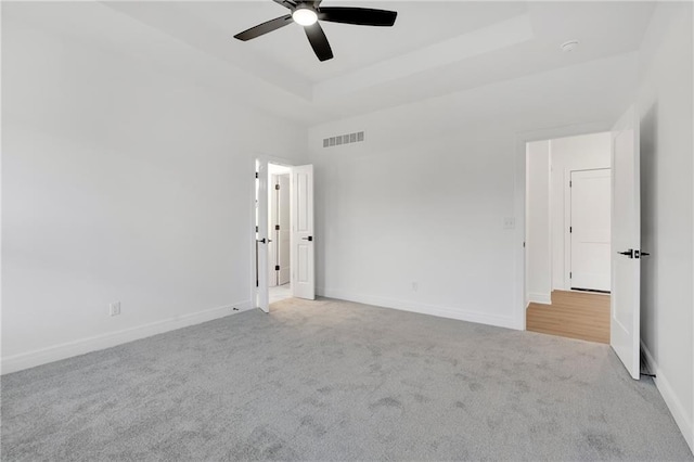 carpeted empty room with baseboards, visible vents, ceiling fan, and a tray ceiling