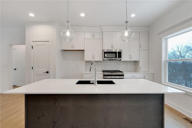 kitchen featuring stainless steel appliances, a sink, white cabinets, light countertops, and tasteful backsplash