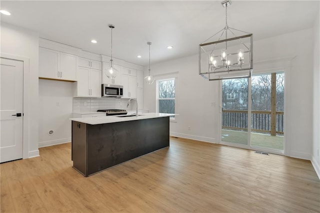 kitchen featuring a sink, white cabinets, light wood-type flooring, tasteful backsplash, and stainless steel microwave