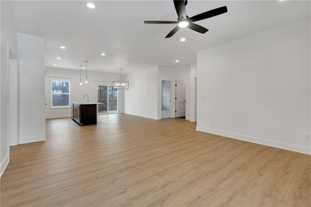 unfurnished living room with light wood-style flooring, ceiling fan with notable chandelier, baseboards, and recessed lighting