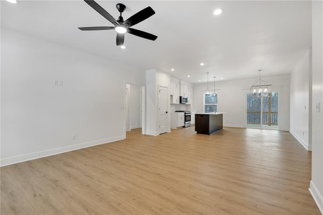 unfurnished living room with recessed lighting, light wood-style flooring, baseboards, and ceiling fan with notable chandelier