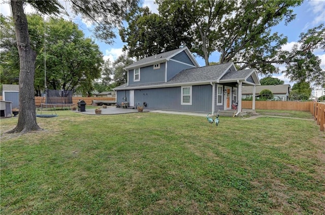 rear view of house with a trampoline, a yard, and a patio