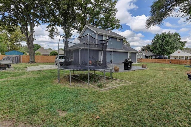 rear view of property featuring a lawn, a trampoline, and a patio area