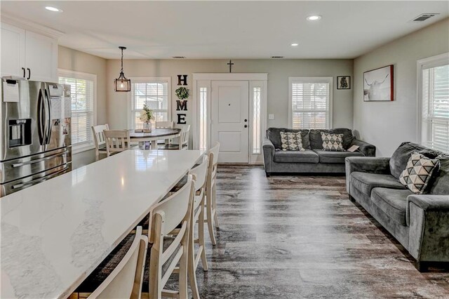 kitchen featuring a breakfast bar, dark hardwood / wood-style floors, white cabinets, decorative light fixtures, and stainless steel fridge