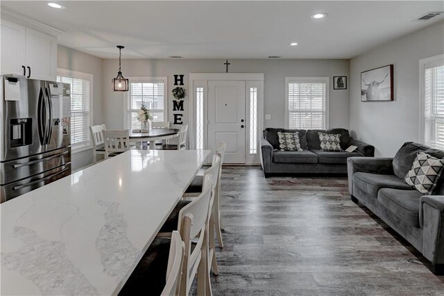 kitchen with light stone counters, stainless steel fridge with ice dispenser, white cabinetry, hanging light fixtures, and a kitchen breakfast bar