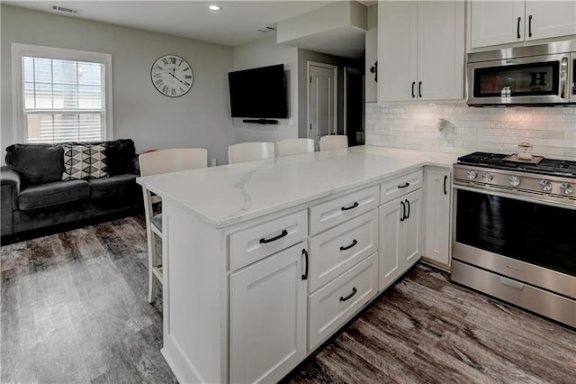 kitchen with light stone counters, white cabinets, kitchen peninsula, stainless steel appliances, and dark hardwood / wood-style flooring