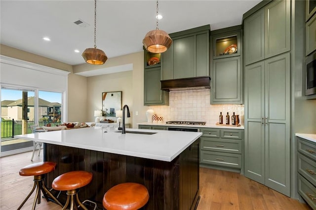 kitchen featuring a kitchen island with sink, a kitchen breakfast bar, light countertops, decorative light fixtures, and green cabinetry