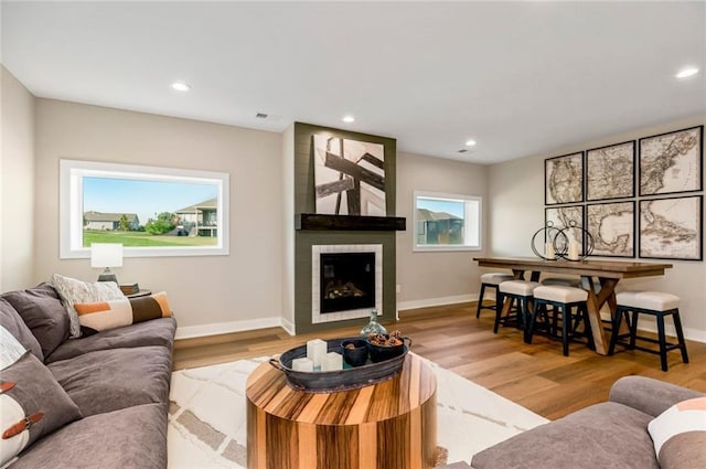 living room featuring light wood-style flooring, a fireplace, baseboards, and recessed lighting