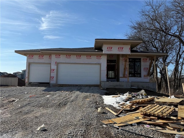 unfinished property with an attached garage and gravel driveway