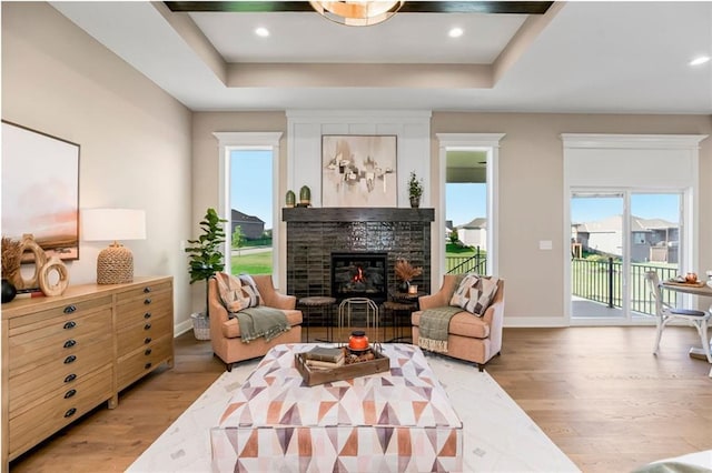living room featuring a raised ceiling, a fireplace, baseboards, and light wood-type flooring