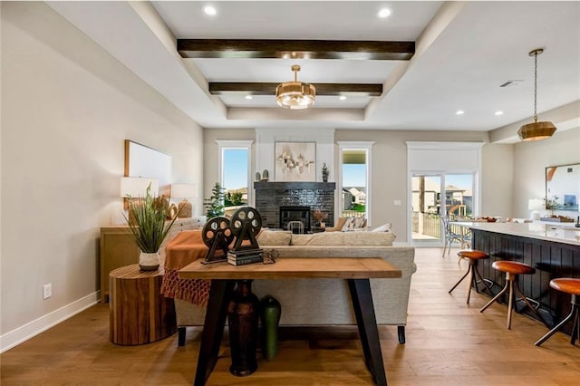 living room with beamed ceiling, a glass covered fireplace, light wood-style flooring, and baseboards