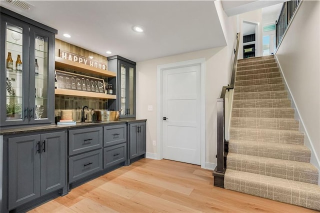 bar featuring stairway, light wood-style flooring, indoor wet bar, and a sink