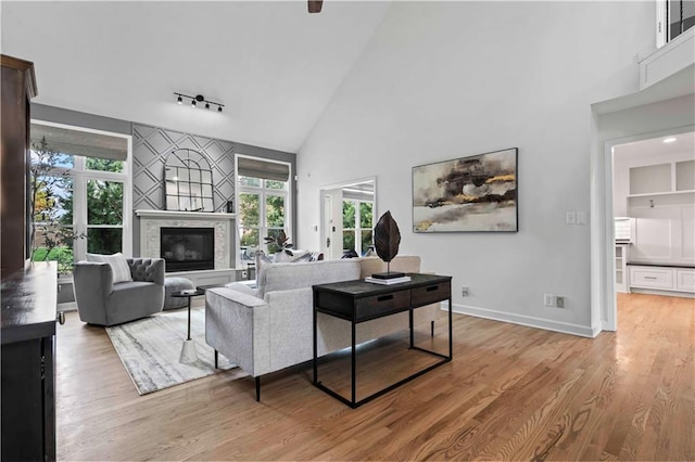 living area with light wood-style flooring, a premium fireplace, high vaulted ceiling, and baseboards