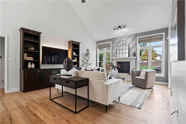 living area with light wood-style floors, baseboards, high vaulted ceiling, and a glass covered fireplace