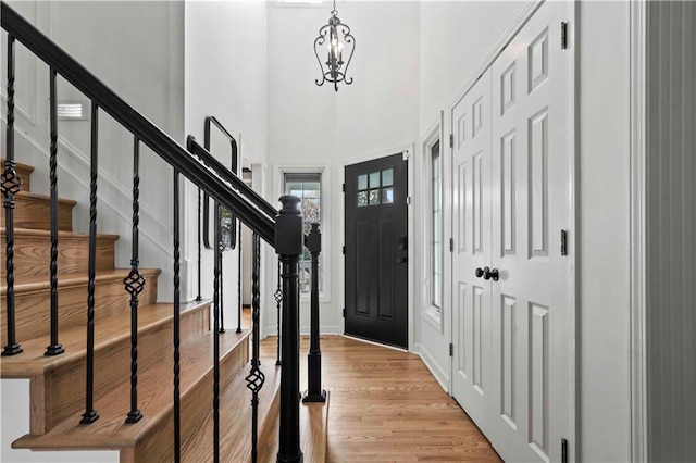 foyer with a chandelier, light wood-style flooring, a high ceiling, baseboards, and stairway