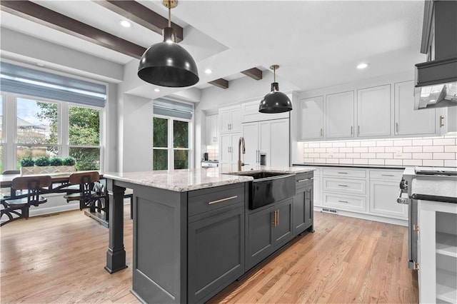 kitchen with light wood finished floors, white cabinetry, decorative backsplash, and a sink