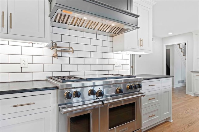 kitchen featuring light wood finished floors, decorative backsplash, dark countertops, custom exhaust hood, and double oven range