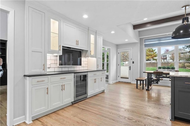 kitchen with beverage cooler, glass insert cabinets, light wood-style flooring, and backsplash