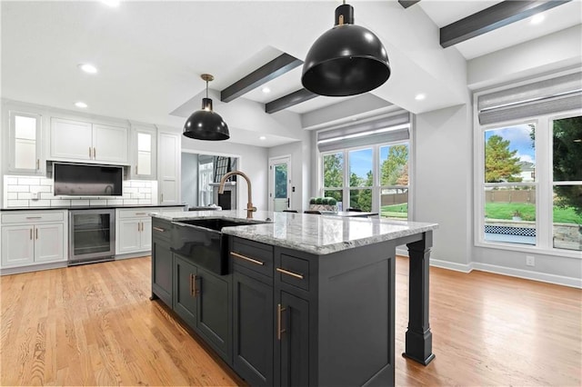 kitchen featuring light wood-style floors, beverage cooler, white cabinetry, and a sink