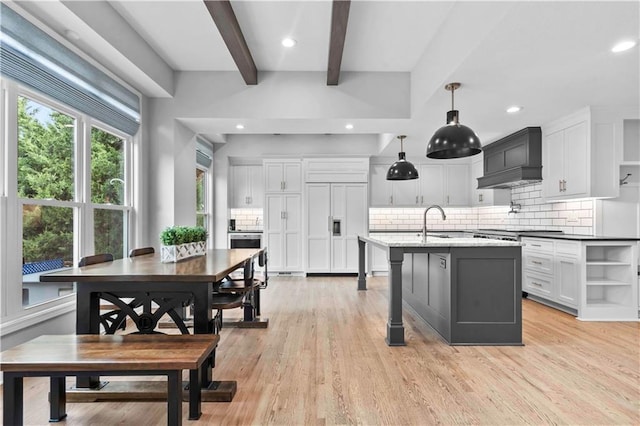 kitchen featuring light wood finished floors, a center island with sink, beam ceiling, and white cabinets