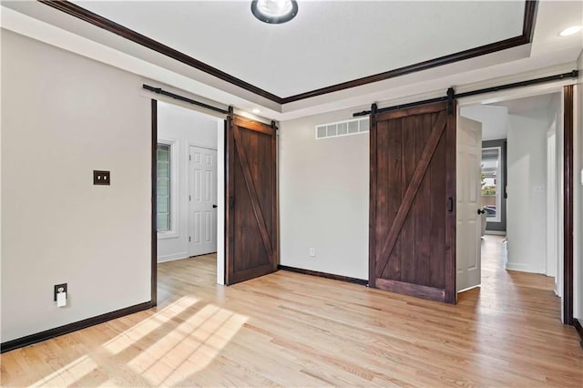 unfurnished bedroom with light wood finished floors, a barn door, a raised ceiling, and visible vents