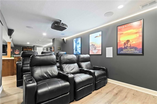 home theater with light wood-type flooring, baseboards, visible vents, and a textured ceiling