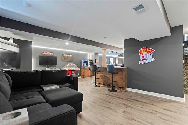 living area with light wood finished floors, a bar, visible vents, and baseboards