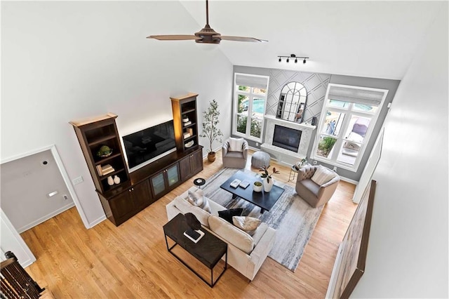 living area with lofted ceiling, rail lighting, light wood-style flooring, a glass covered fireplace, and baseboards