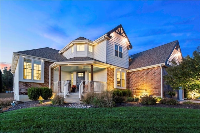 view of front of home featuring a yard, a shingled roof, a porch, and brick siding