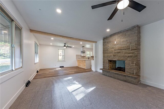 unfurnished living room featuring a stone fireplace, ceiling fan, beamed ceiling, and hardwood / wood-style flooring