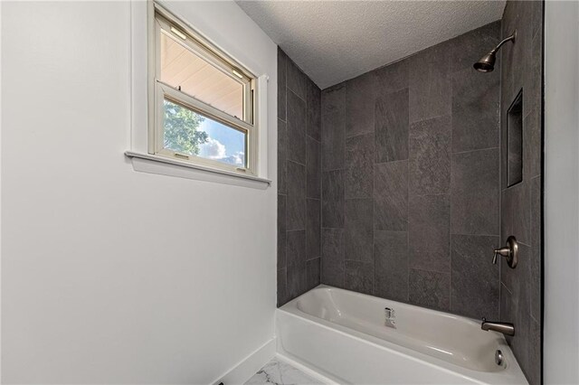 bathroom with a textured ceiling and tiled shower / bath