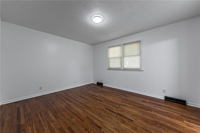 spare room with a textured ceiling and dark hardwood / wood-style flooring