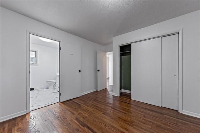 unfurnished bedroom featuring ensuite bath, a closet, dark hardwood / wood-style floors, and a textured ceiling