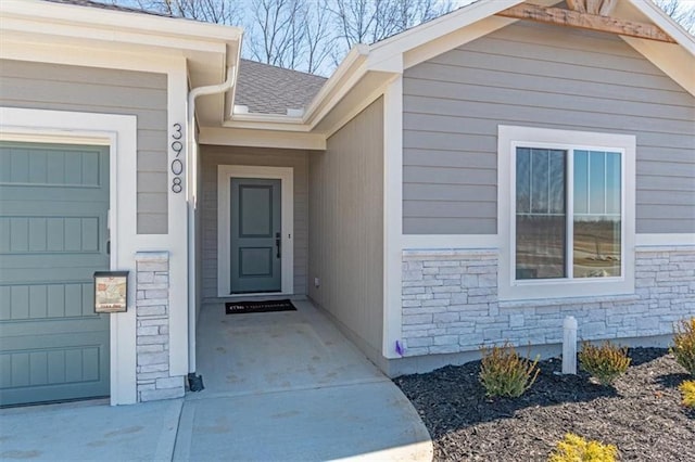 property entrance featuring stone siding, a shingled roof, and an attached garage