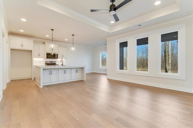 unfurnished living room with a sink, baseboards, light wood-style floors, a tray ceiling, and crown molding