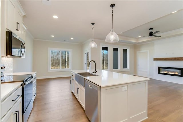 kitchen featuring crown molding, stainless steel appliances, open floor plan, white cabinetry, and light wood-type flooring