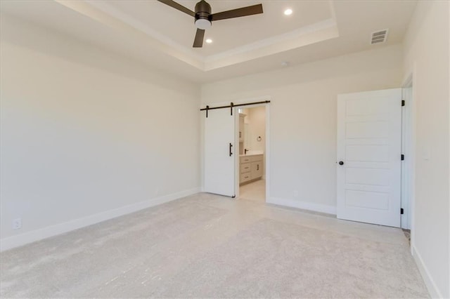 unfurnished bedroom featuring a barn door, baseboards, a raised ceiling, light colored carpet, and recessed lighting