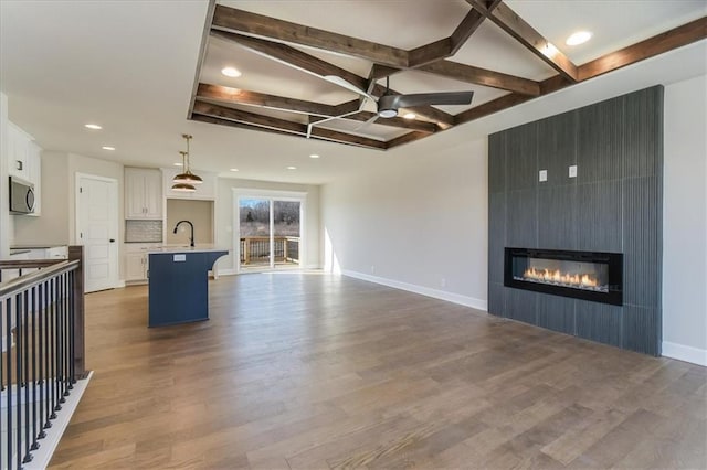 unfurnished living room featuring a large fireplace, coffered ceiling, wood finished floors, and baseboards