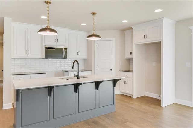 kitchen featuring a center island with sink, stainless steel microwave, hanging light fixtures, light wood-type flooring, and a sink