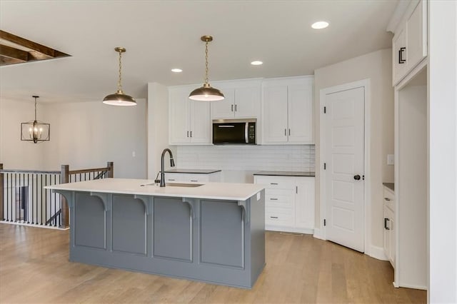 kitchen with light wood finished floors, stainless steel microwave, a sink, and white cabinets