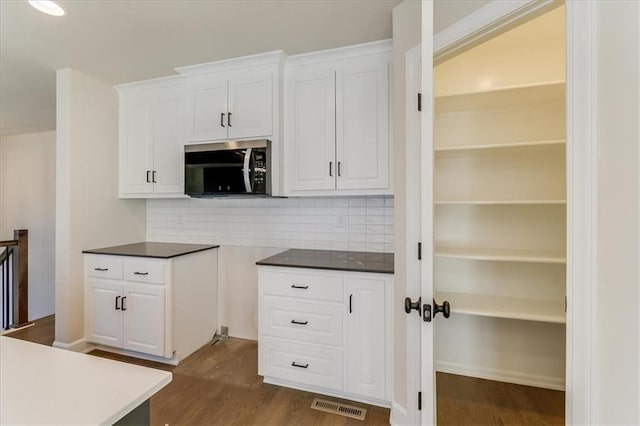 kitchen featuring dark wood finished floors, tasteful backsplash, stainless steel microwave, visible vents, and white cabinets