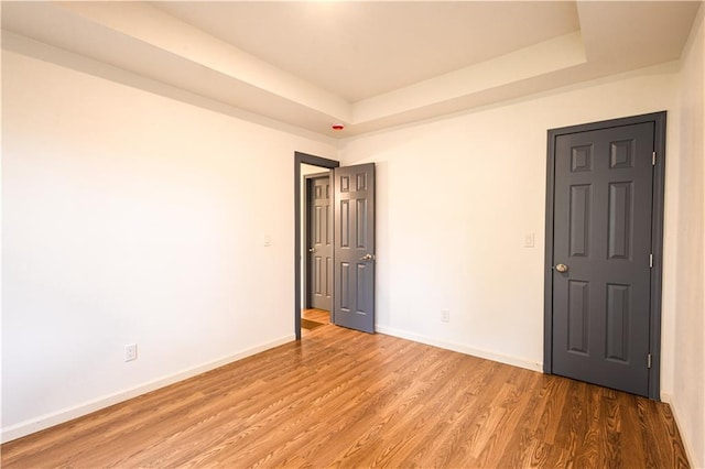 unfurnished bedroom featuring wood-type flooring and a tray ceiling