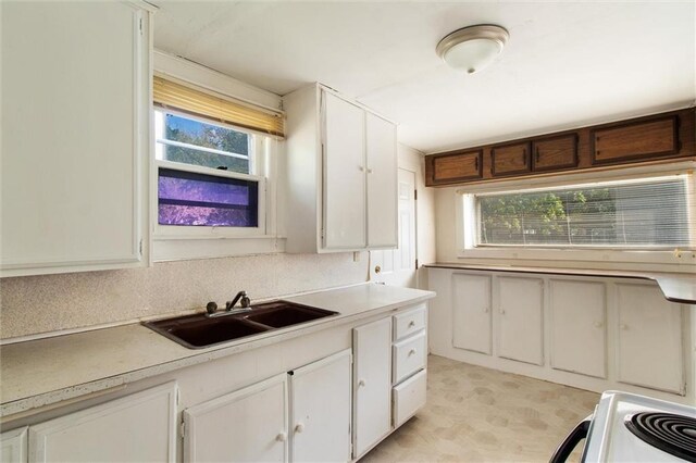 kitchen with white cabinets, stove, sink, and a wealth of natural light