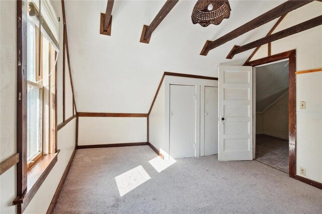 unfurnished bedroom featuring lofted ceiling with beams, a closet, and light colored carpet